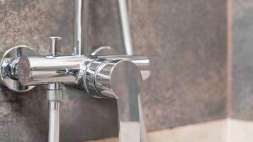 A chrome faucet with a single handle and a spout, mounted on a tiled wall.