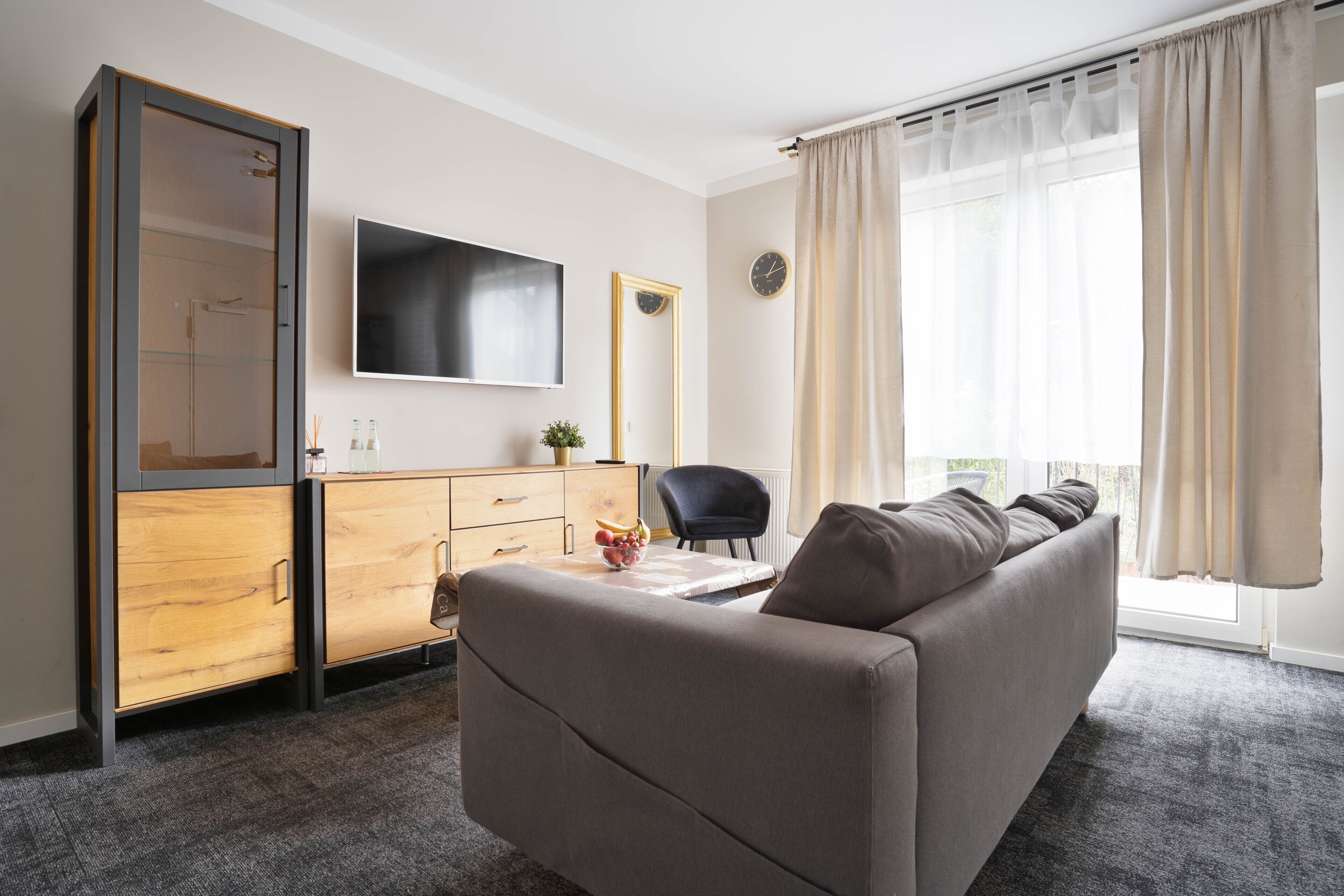 Een moderne woonkamer met een bank, een televisie, een houten kast en een groot raam met gordijnen.