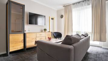 Een moderne woonkamer met een bank, een televisie, een houten kast en een groot raam met gordijnen.