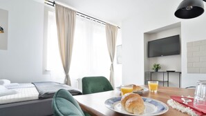 A modern hotel room with a bed, breakfast table with croissant and juice, a TV, and a window with curtains. - Stilvolle Apartments in Bonn I home2share (Bonn)