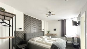 A modern hotel room with a bed, a desk, a chair, a TV, and a wardrobe. - Stilvolle Apartments in Bonn I home2share (Bonn)
