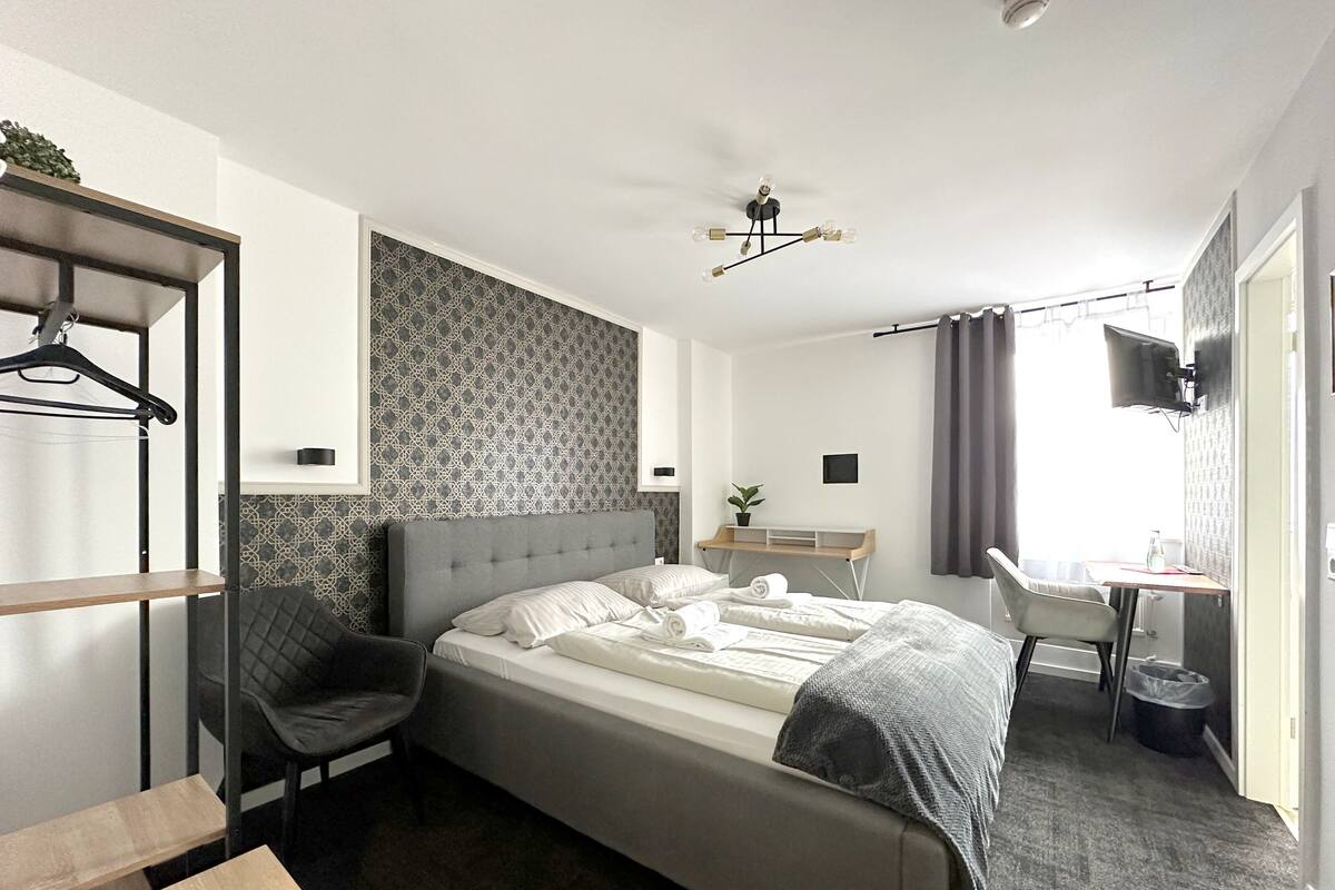 Een moderne hotelkamer met een bed, een bureau, een stoel, een televisie en een garderobe.