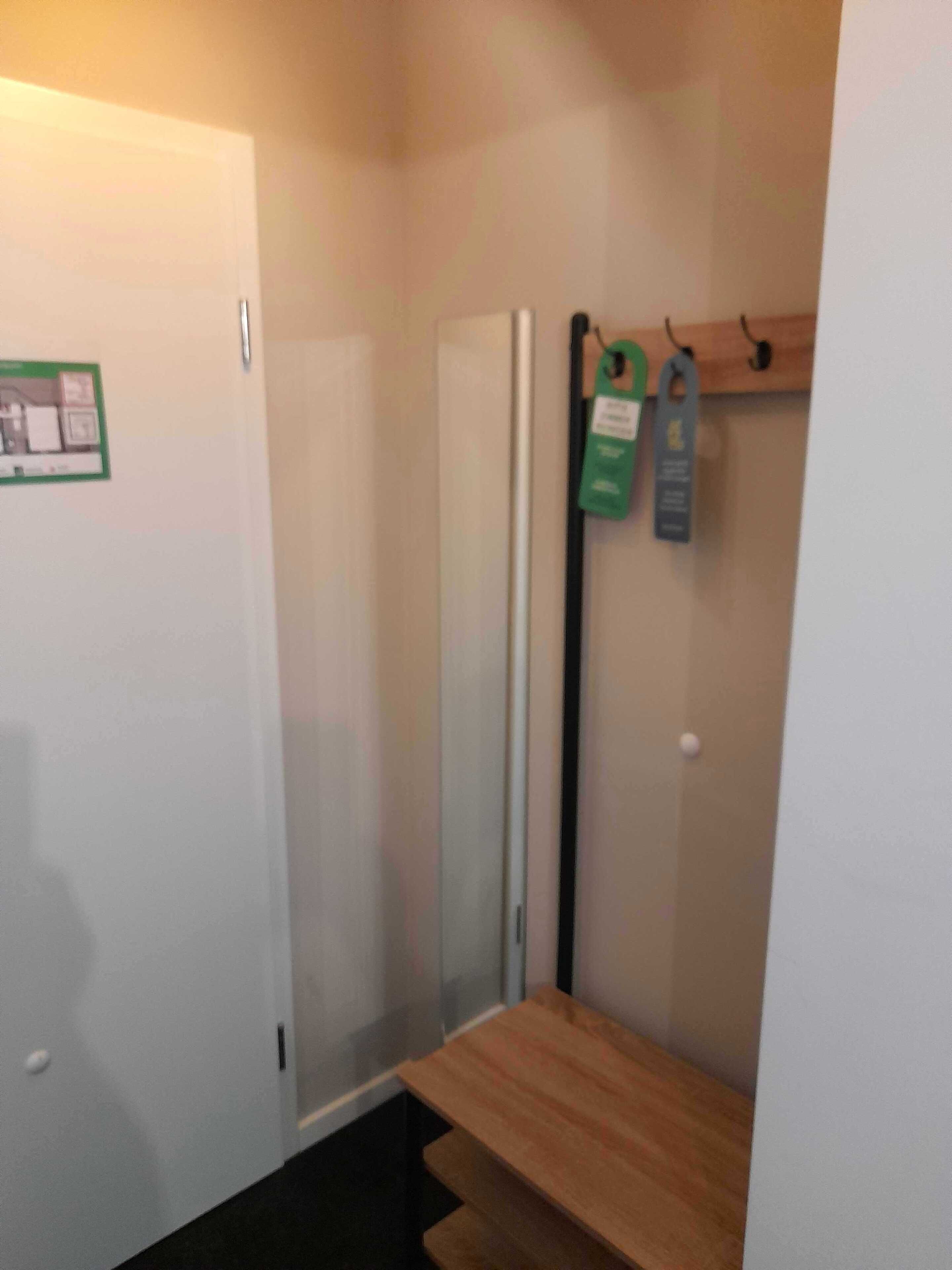 Un couloir étroit avec un banc en bois, une porte ornée d’une enseigne verte et un poteau vertical recouvert d’étiquettes.