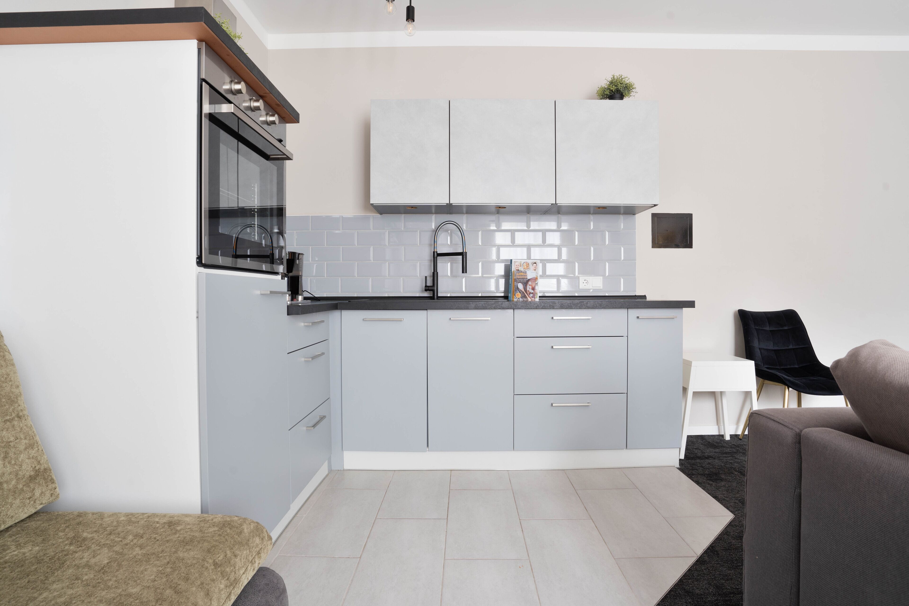 A modern kitchen with grey cabinets, a black countertop, and a black chair.