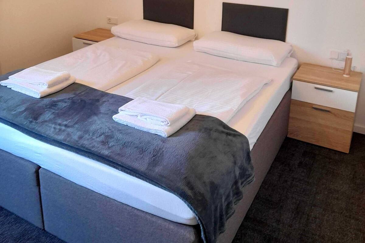 Een hotelkamer met een bed, twee nachtkastjes, een wandlamp en een kunstwerk met een stadsgezicht boven het bed.