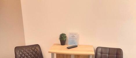 Une petite pièce avec deux fauteuils en cuir marron, un bureau en bois orné d’une plante et d’une télécommande, et une horloge murale.