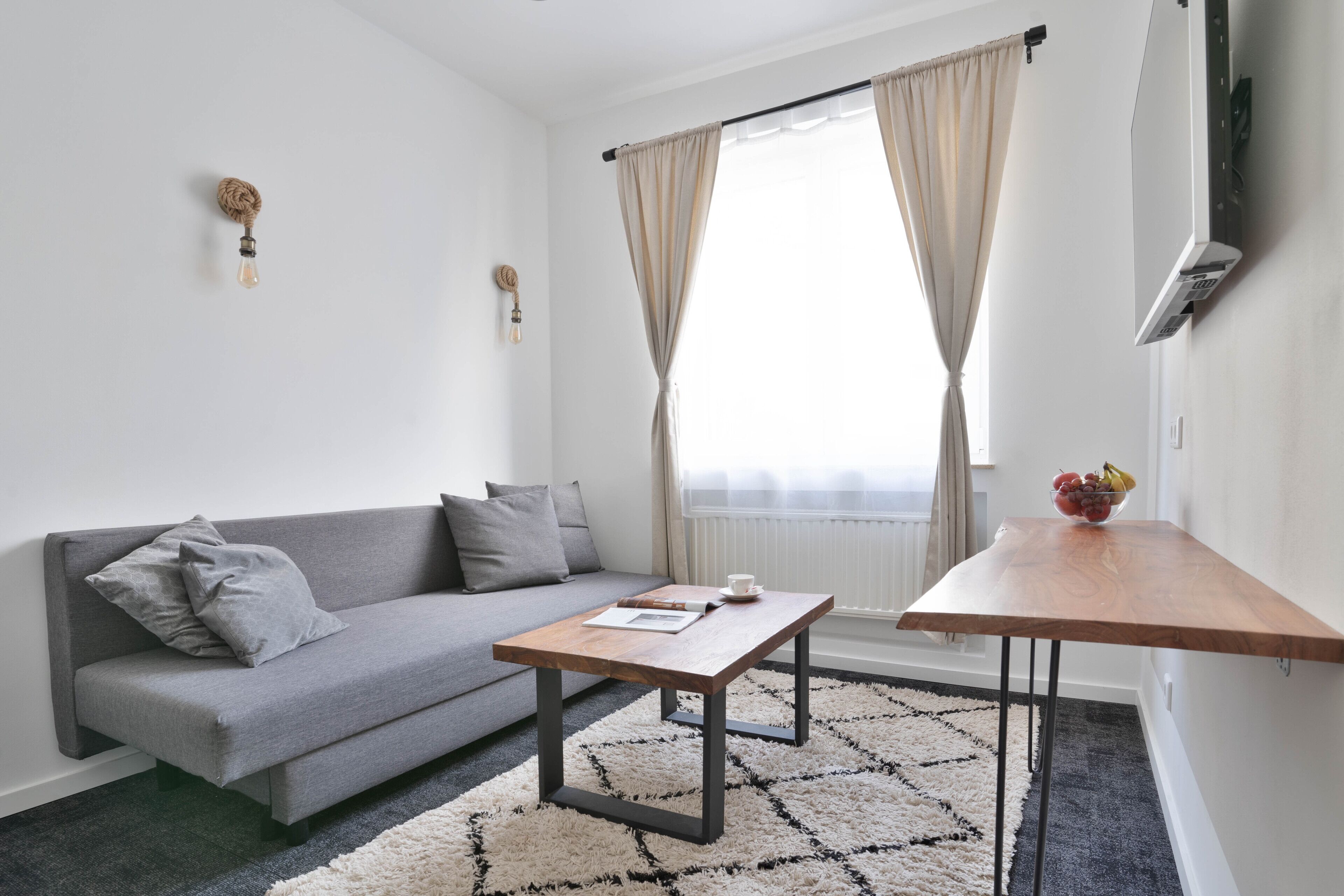 A modern living room with a grey sofa, a wooden coffee table, and a patterned rug.