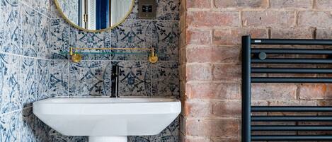 A bathroom with a white pedestal sink, a round mirror with a gold frame, and a black radiator.