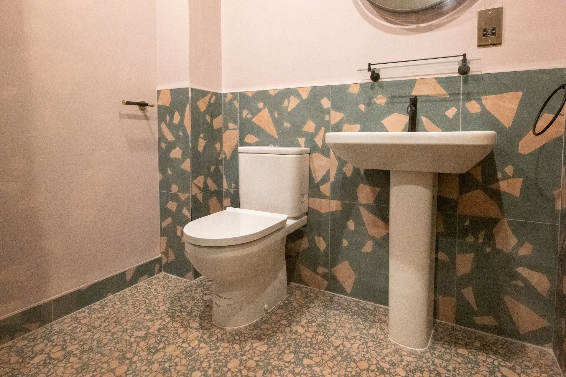 Ein Badezimmer mit Toilette, Waschbecken und gemusterten Fliesen.