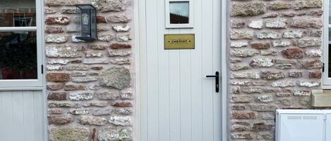 A stone building with a white door, a small window, and a sign above the door.