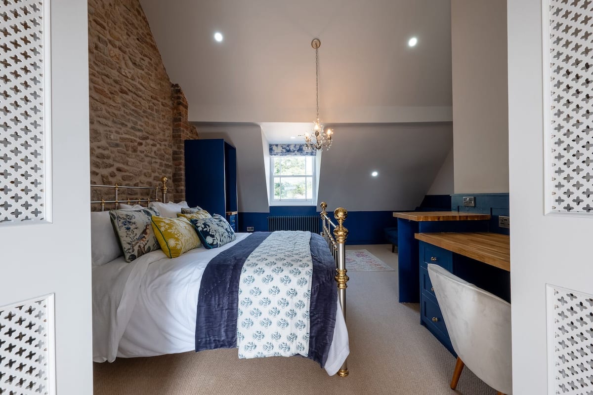 A bedroom with a sloped ceiling, a bed with patterned bedding, a chandelier, and a desk area.