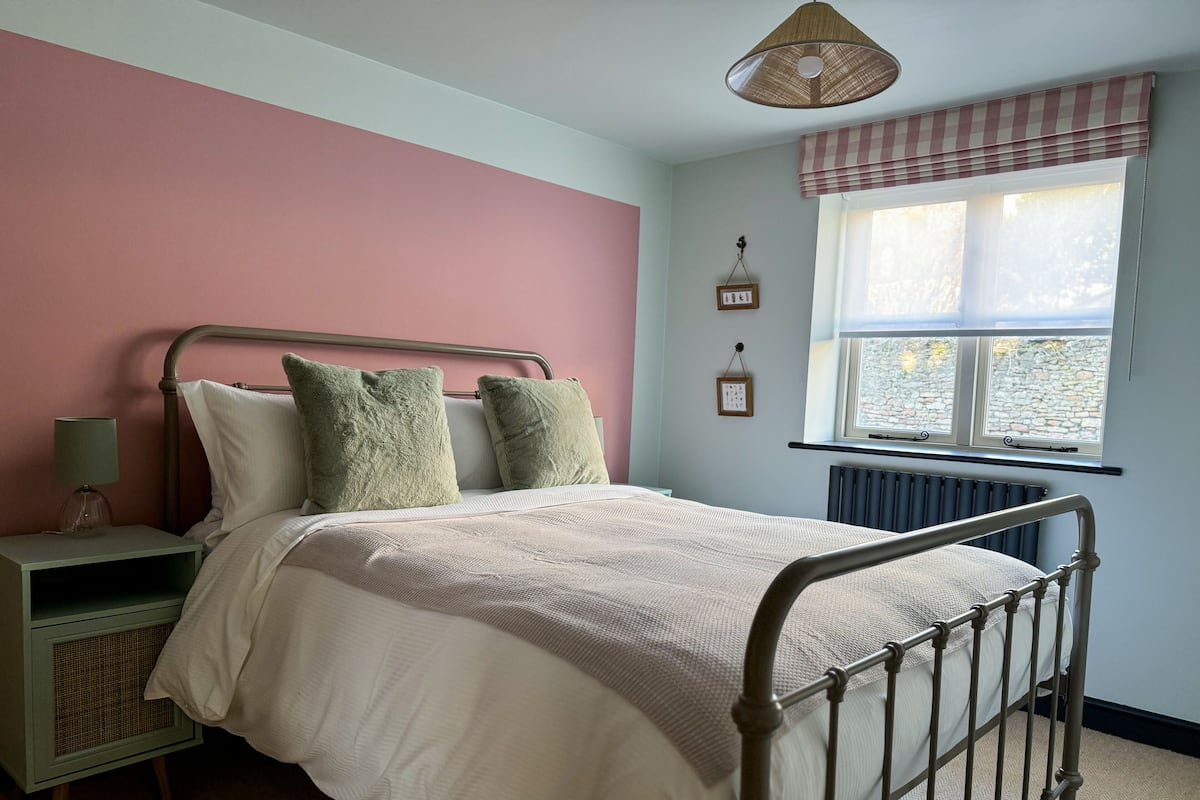 A bedroom with a metal bed frame, a bedside table with a lamp, a window with a view of the outside, and a radiator.