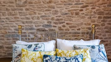 Una cama con estructura metálica y detalles dorados ornamentales, frente a una pared de piedra.