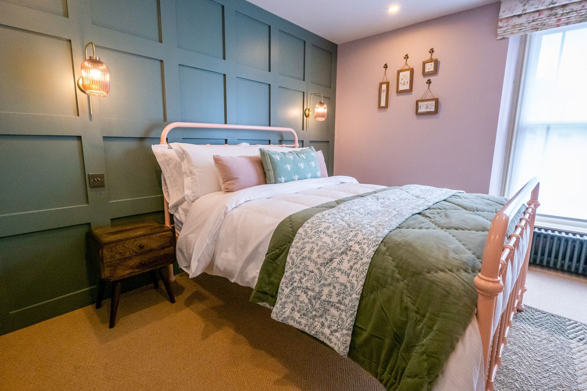 A bedroom with a bed, bedside table, wall-mounted light, and framed pictures.