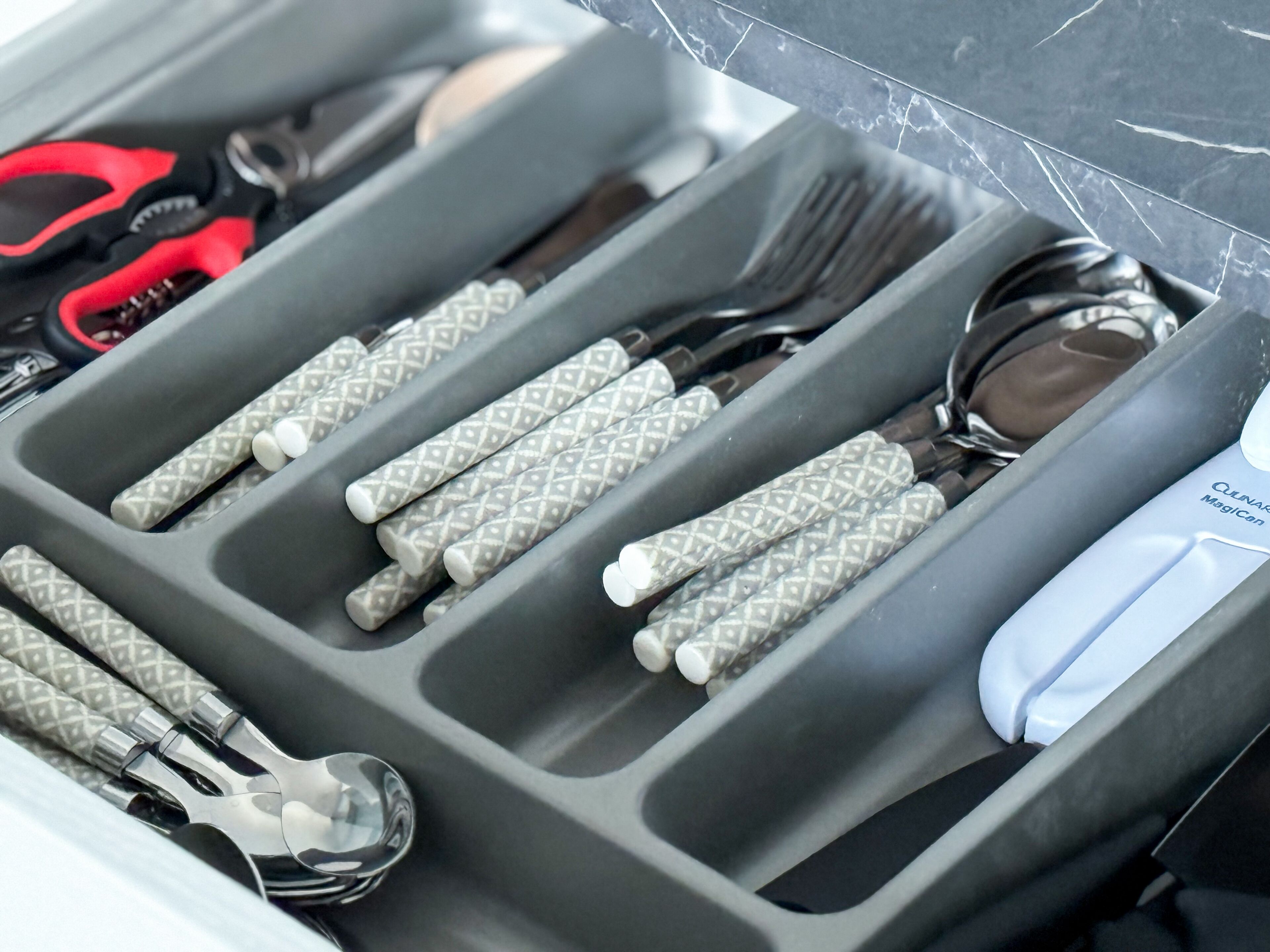 A drawer with compartments containing various utensils and a spoon.