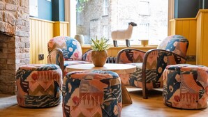 A cozy seating area with patterned ottomans and chairs, a round wooden table, and a potted plant.