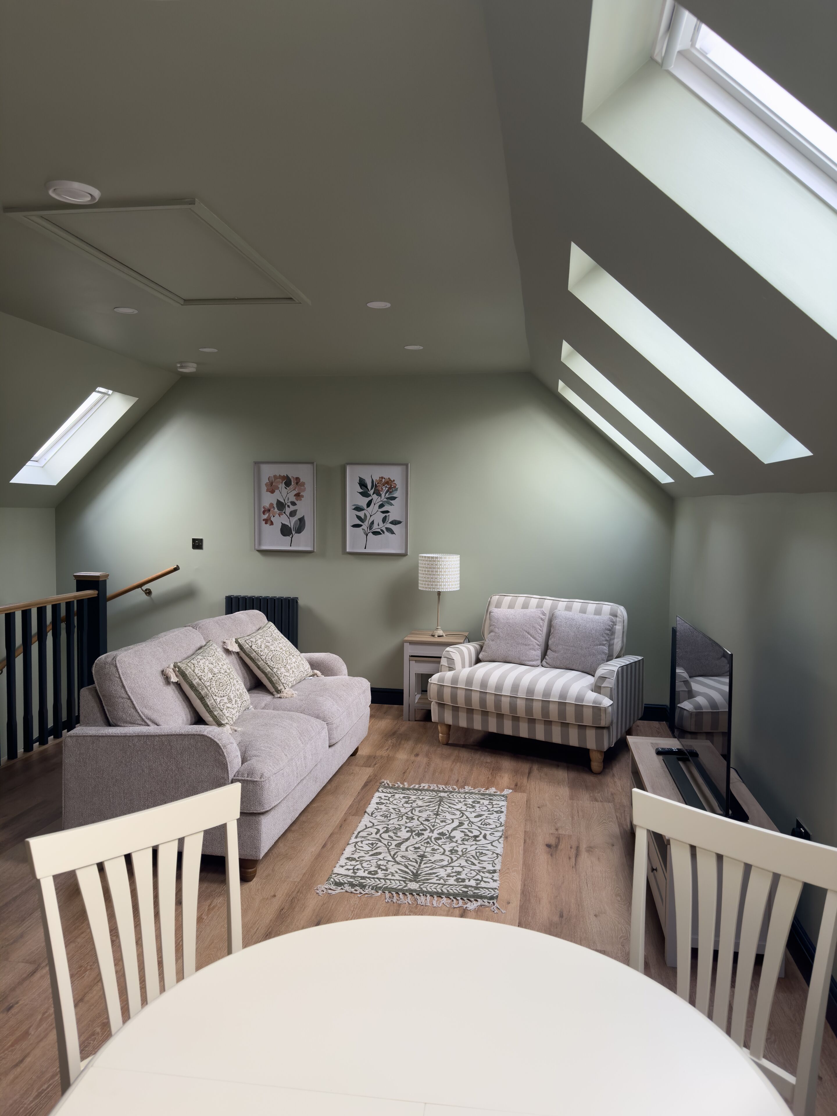 Une pièce de style « loft », avec un plafond haut, des fenêtres de toit, un canapé, un fauteuil, une petite table et un téléviseur.