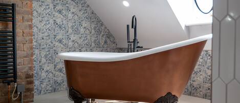 A freestanding bathtub in a modern bathroom with a sloped ceiling and patterned tile walls.