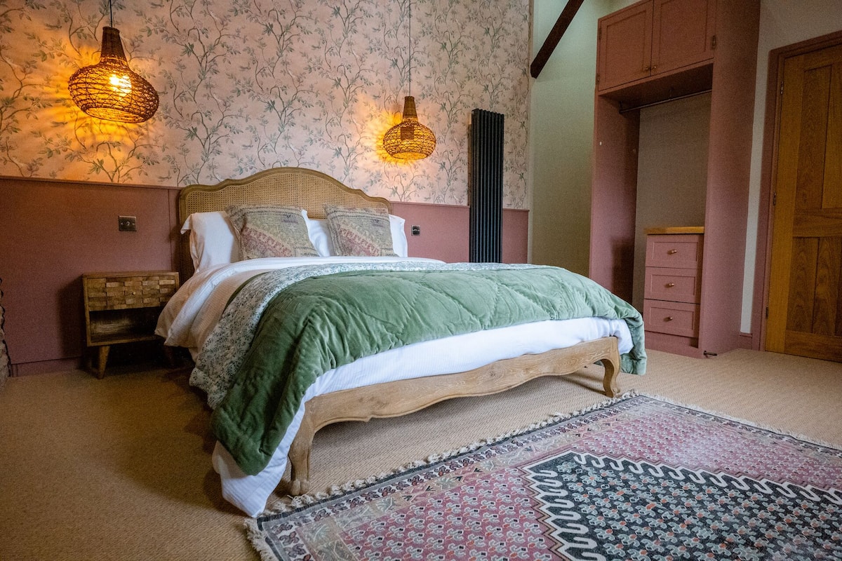 A bedroom with a wooden bed, two wall-mounted lamps, a patterned rug, and a small bedside table.