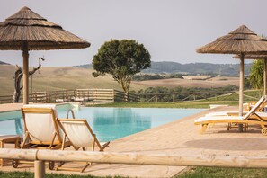 A poolside area with lounge chairs and thatched umbrellas, surrounded by a wooden fence and a view of rolling hills. - Le Fraine Agriturismo & Olives Glamping (Santa Luce)