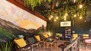 A cozy lounge area with wicker furniture, a mural of a mountain landscape, and a bookshelf. - Forrest Hostels (Mumbai)