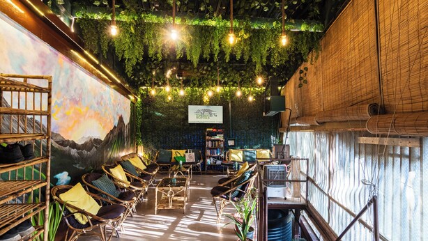 A cozy lounge area with wicker chairs, a mural, and hanging plants. - Forrest Hostels (Mumbai)