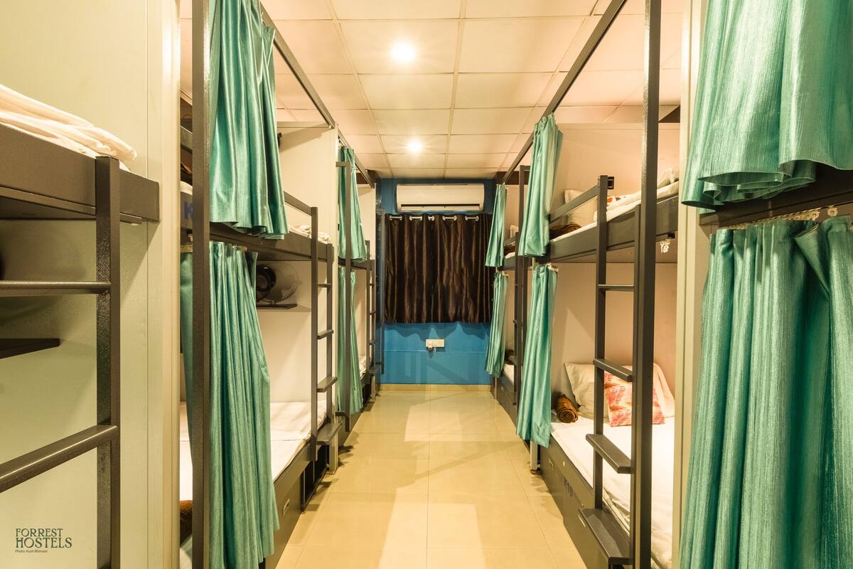 A corridor with bunk beds, each with a curtain. The corridor has a tiled floor and a blue wall at the end.