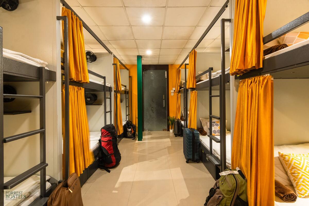 A corridor with bunk beds, each with orange curtains, and a green pillar in the center.