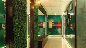 A hallway with green walls, a bench, and framed pictures. - Forrest Hostels (Mumbai)