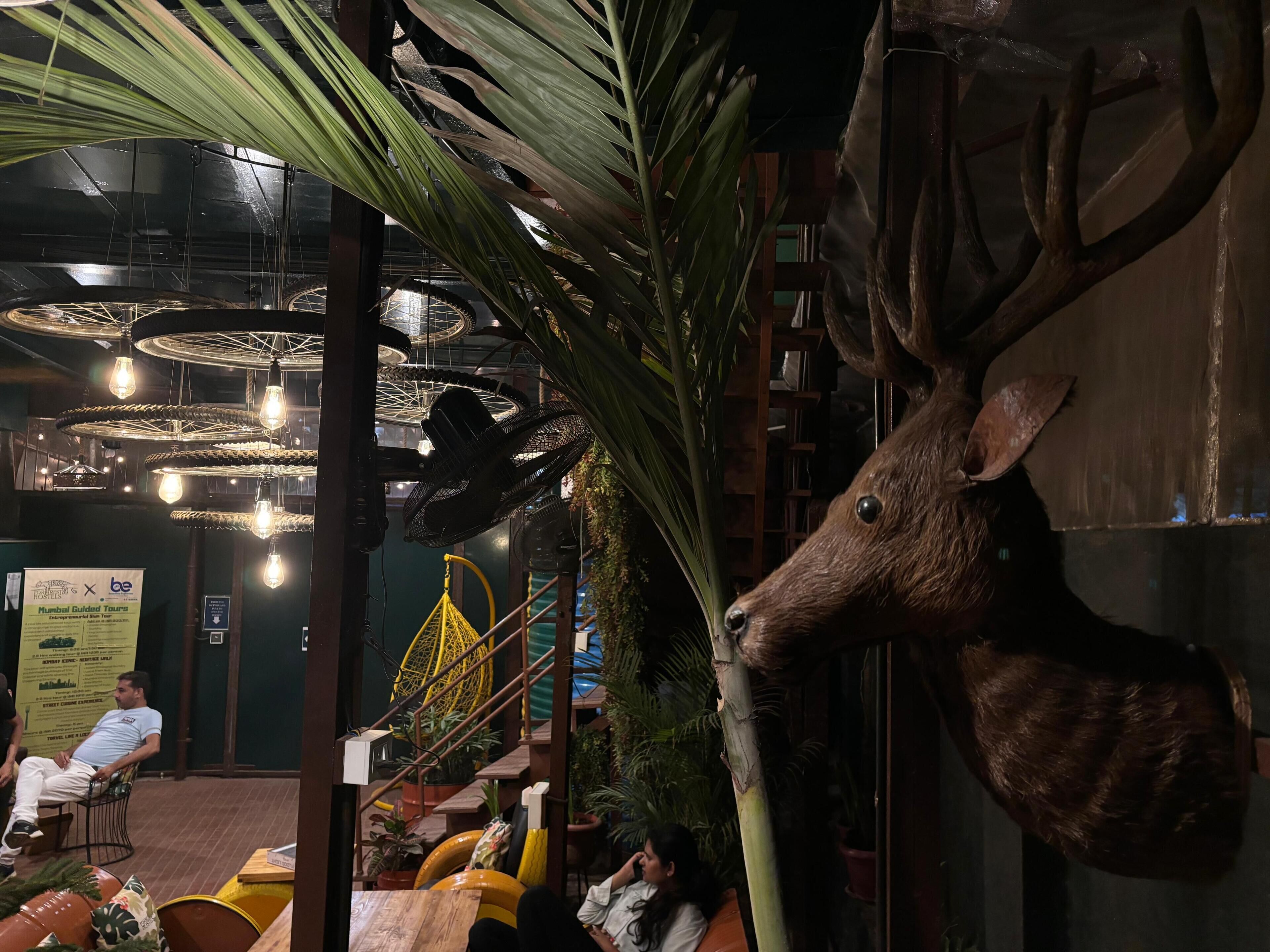 A restaurant with a unique decor including a deer head sculpture, hanging lights, and a yellow swing chair.