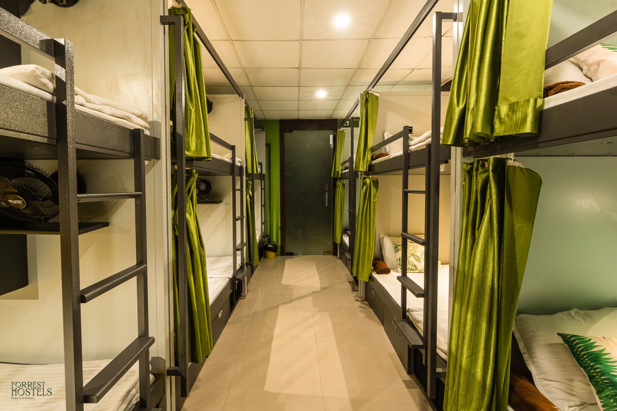 A narrow corridor with bunk beds on either side, each with green curtains.