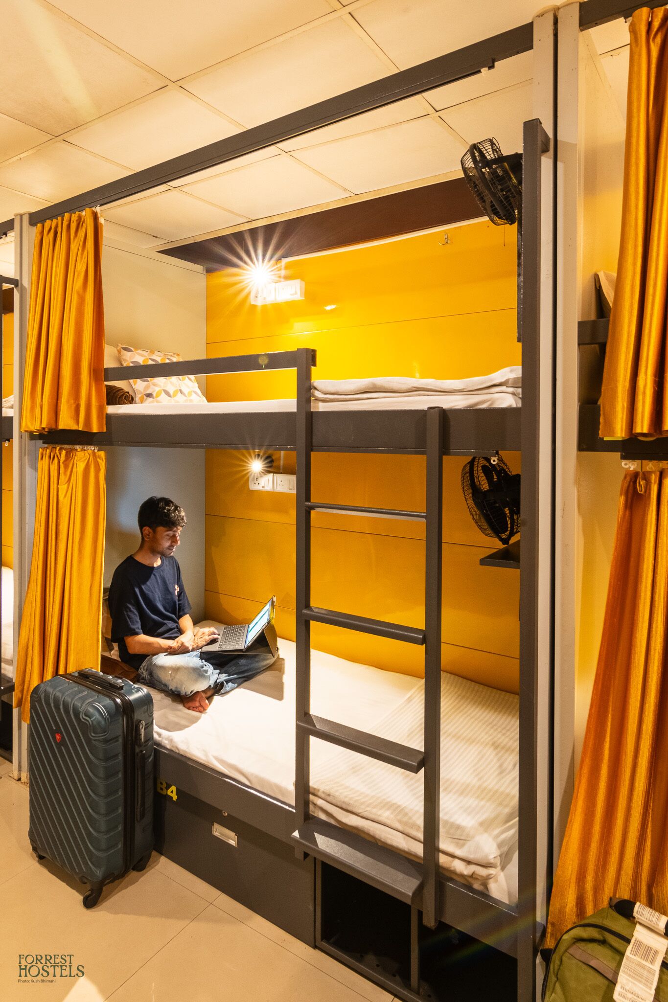 A bunk bed room with a laptop on the lower bunk, a suitcase, and a green backpack.