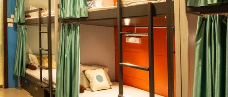 Bunk beds with green curtains, a tiled floor, and a wall-mounted shelf.