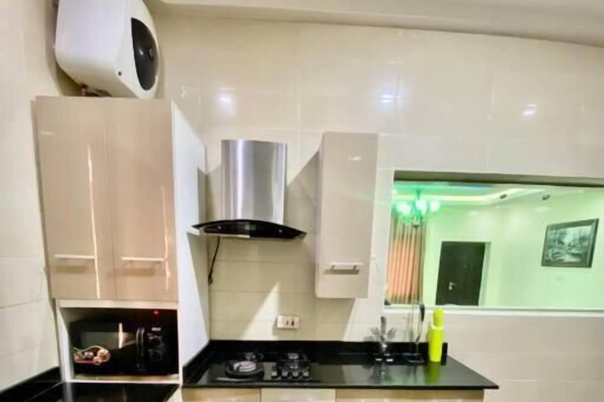 A modern kitchen with a black countertop, beige cabinets, a stainless steel range hood, and a window with a green tint.