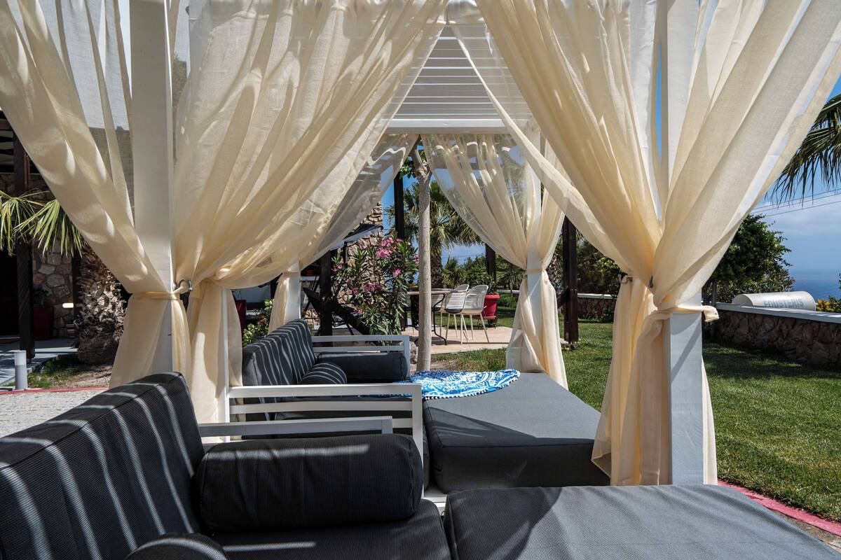 An outdoor seating area with white canopies, cushioned sofas, and a stone wall backdrop.