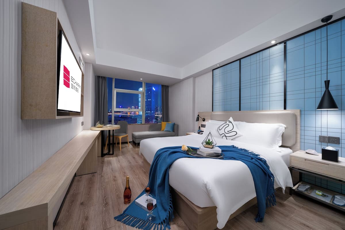 Ein modernes Hotelzimmer mit einem großen Bett, einem Schreibtisch, einem Sessel und einem an der Wand befestigten Fernseher.