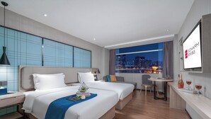 Una habitación de hotel moderna con una cama grande, un escritorio, una silla y vistas a la ciudad.