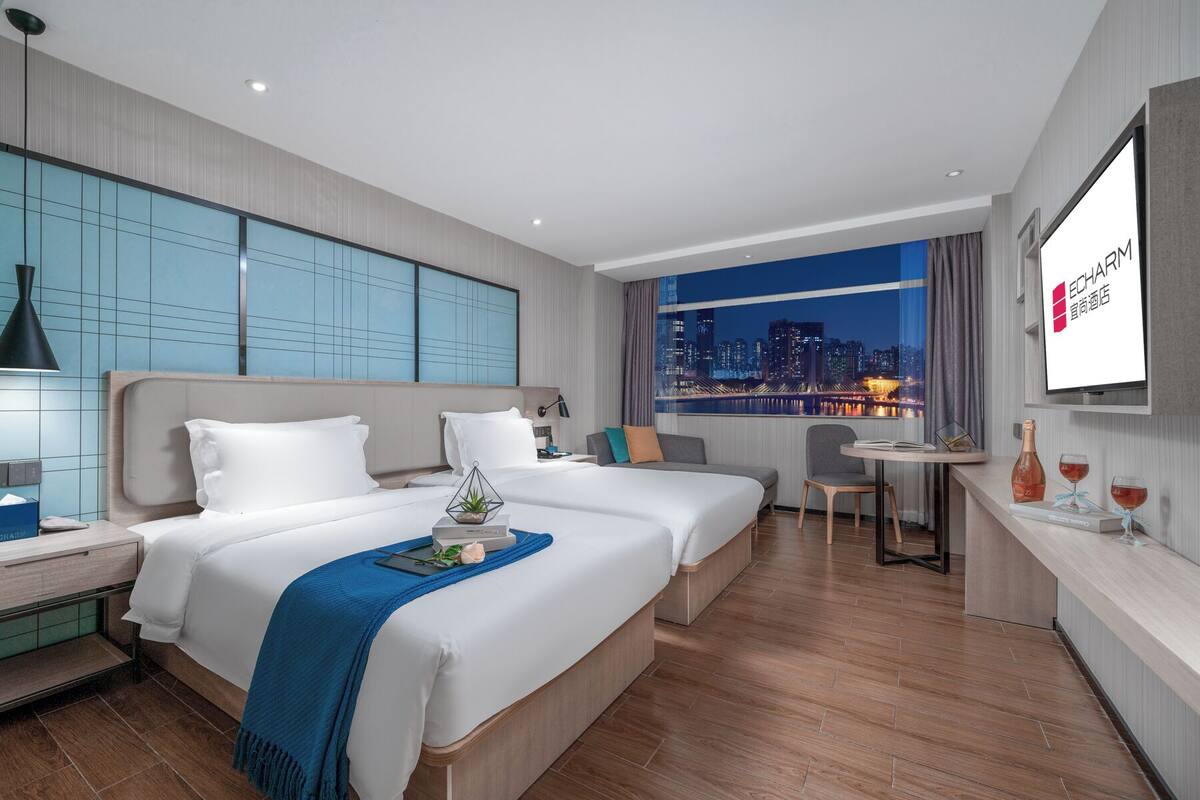 Ein modernes Hotelzimmer mit einem großen Bett, einem Schreibtisch, einem Sessel und Blick auf die Stadt.