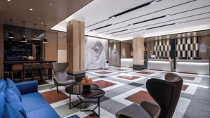 Un vestíbulo moderno con suelo a cuadros, zona de estar con sofás y sillones, mostrador de recepción y área de bar.