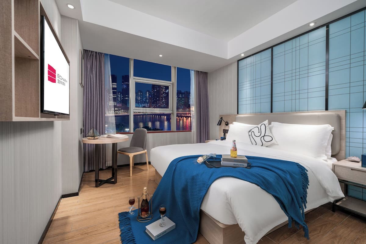 Ein modernes Hotelzimmer mit einem großen Bett, einem Schreibtisch und Blick auf nächtliche Stadtansichten.