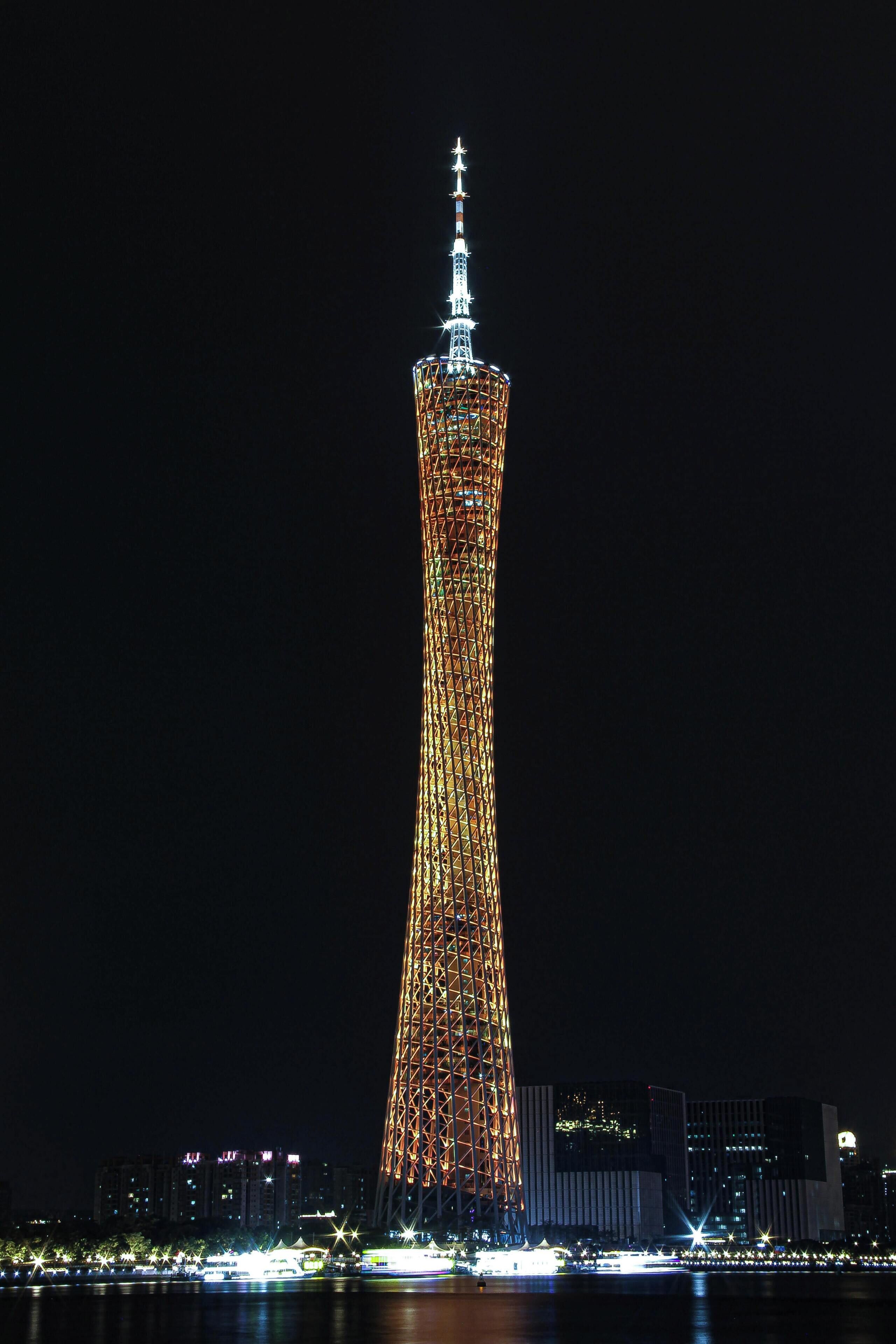 Una torre alta e iluminada con un diseño retorcido único, rodeada de luces de la ciudad y edificios.