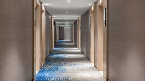 Un largo y estrecho pasillo de hotel con alfombra estampada, paneles de madera en las paredes e iluminación empotrada.