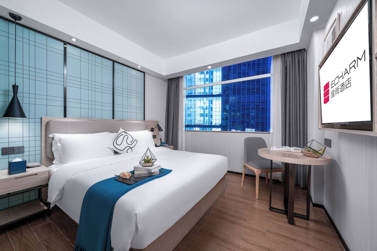 Ein modernes Hotelzimmer mit einem großen Bett, einem Schreibtisch und einem Fenster mit Blick auf die Stadt.