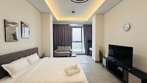 A modern hotel room with a large bed, a sofa, a TV, and a view of the city through the window. - Upscale Studio Apartment Palm View with Big Balcony Free Parking by Belvilla (Dubai)