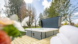 Un bain à remous sur une terrasse en bois, avec vue sur les arbres et une maison en arrière-plan.