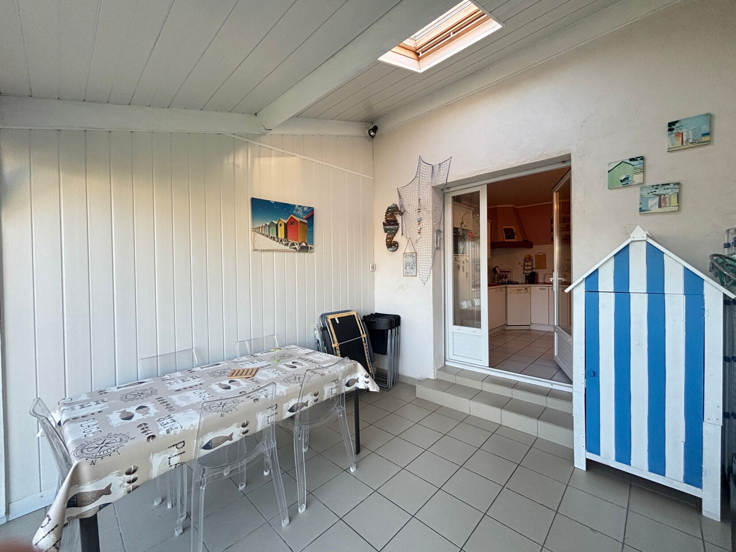 A dining area with a table set for four, a kitchen visible through an open door, and a blue and white striped structure.