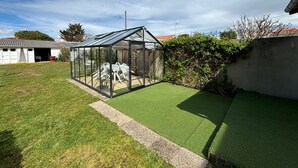 A greenhouse with a glass roof and walls, surrounded by a well-maintained lawn and a white building in the background. - Charming 2-Bedroom House with Garden Near Beach and Port Olona (Les Sables-d'Olonne)