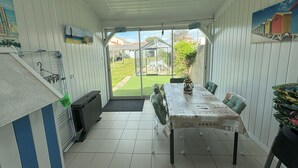 A dining area with a table set for four, a view of the backyard, and a window with a view of houses and greenery. - Charming 2-Bedroom House with Garden Near Beach and Port Olona (Les Sables-d'Olonne)