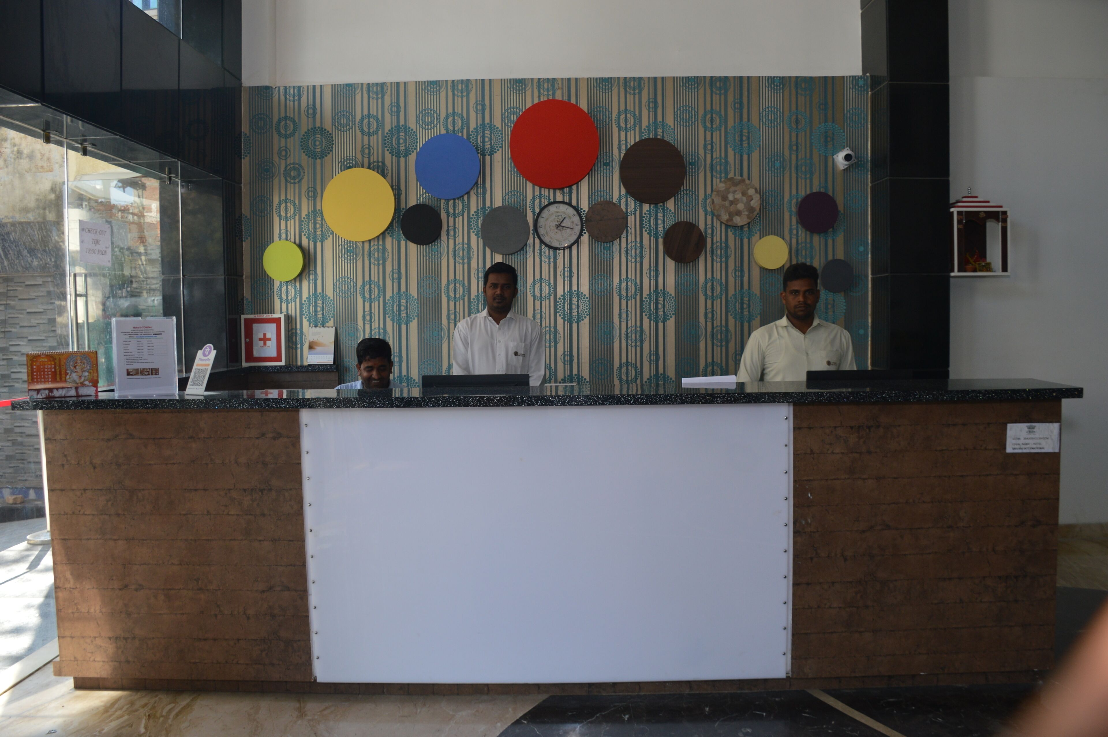 A reception desk with a patterned wall behind it, a clock, and a small shelf with a decorative item.
