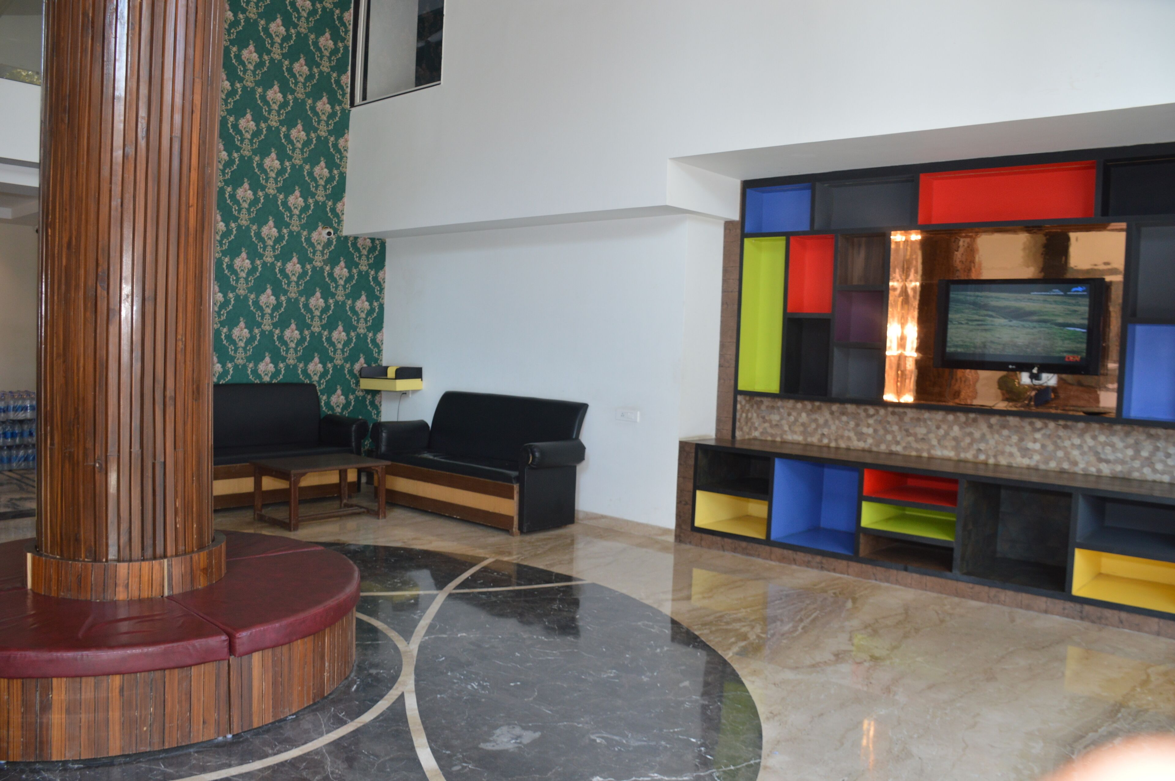 Un vestíbulo con una columna de madera, un sofá de cuero negro y un televisor sobre una estantería colorida.